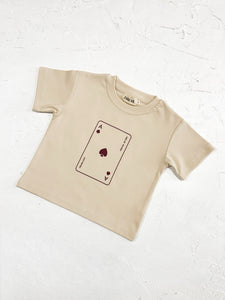 Flat lay of a cream-colored t-shirt with "Lucky Ace" design, paired with neutral accessories.

