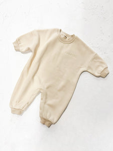 Baby in cream ribbed all-in-one romper, lounging comfortably on a blanket.

