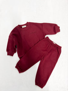 Two-piece kids set in burgundy laid out on a  neutral-toned background for a warm, inviting look.

